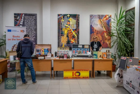 Посетител разглежда книги, изложени в отворени куфари на издателски щанд.
