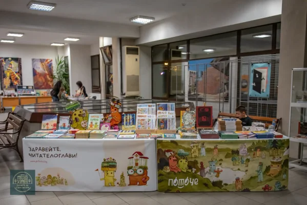 Щанд с детски книги, илюстрована покривка и цветни стойки за изданията.